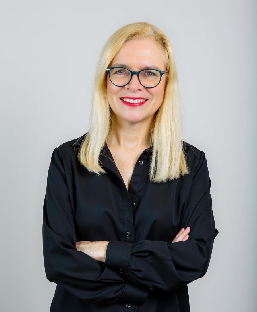 Bonnie Ann, arms folded, in a black shirt against a pale grey background